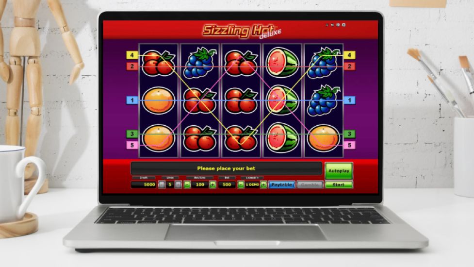 Laptop pokazujący slot Sizzling Hot Deluxe z tradycyjnym motywem owoc&oacute;w i 5 liniami wypłat.